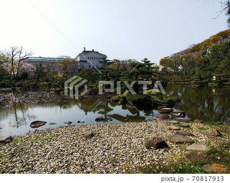 手前に飛び石や島がある日本庭園の池の向こうに桜の木と洋風建築の写真素材