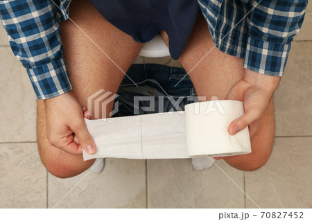 A man sits on the toilet and hold toilet paper A man sits on the toilet and hold toilet paper 70827452