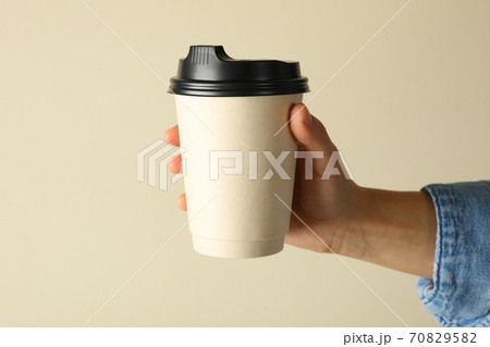 Female hand hold paper cup of coffee on beige background 70829582