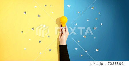 Person holding a yellow light bulb with stars 70833044