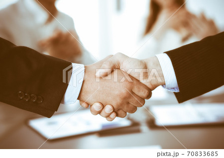Business people shaking hands at meeting while theirs colleagues clapping and applauding. Group of unknown businessmen and women in modern white office. Success teamwork, partnership and handshake Business people shaking hands at meeting while theirs colleagues clapping and applauding. Group of unknown businessmen and women in modern white office. Success teamwork, partnership and handshake 70833685