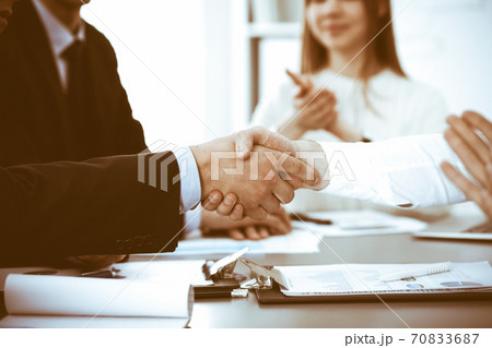 Business people shaking hands at meeting while theirs colleagues clapping and applauding. Group of unknown businessmen and women in modern white office. Success teamwork, partnership and handshake Business people shaking hands at meeting while theirs colleagues clapping and applauding. Group of unknown businessmen and women in modern white office. Success teamwork, partnership and handshake 70833687