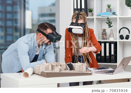 Two young architects in VR glasses working with layout of a residential area in modern office. 70835916