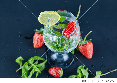 A glass of juice with whole fruits and slice of lemon inside on dark background 70836475