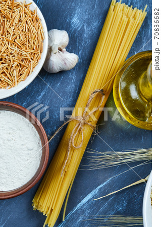 Various uncooked pasta with a bottle of oil, flour, and garlic on a blue background Various uncooked pasta with a bottle of oil, flour, and garlic on a blue background 70836682