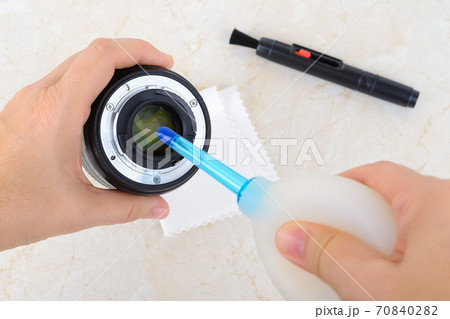 Hands blowing off dust from rear lens using silicone air blower. 70840282