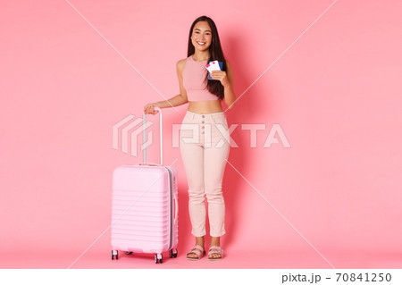 Travelling, holidays and vacation concept. Full-length of cheerful smiling asian girl tourist with suitcase, holding passport with flight tickets, heading to aiport to start journey, pink background Travelling, holidays and vacation concept. Full-length of cheerful smiling asian girl tourist with suitcase, holding passport with flight tickets, heading to aiport to start journey, pink background 70841250