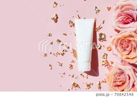 Natural organic cosmetic packaging mockup, pieces of golden paper and pink roses on pastel pink table. Blank white tube design mockup, top view. Spa cosmetic product. 70842548