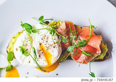 Toast with salmon, poached egg and avocado on white plate, top view. Poached egg with salmon and guacamole on rye bread. Toast with salmon, poached egg and avocado on white plate, top view. Poached egg with salmon and guacamole on rye bread. 70848187