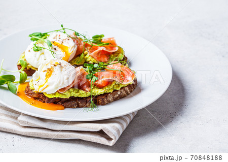 Toast with salmon, poached egg and avocado on white plate. Poached egg with salmon and guacamole on rye bread. Toast with salmon, poached egg and avocado on white plate. Poached egg with salmon and guacamole on rye bread. 70848188