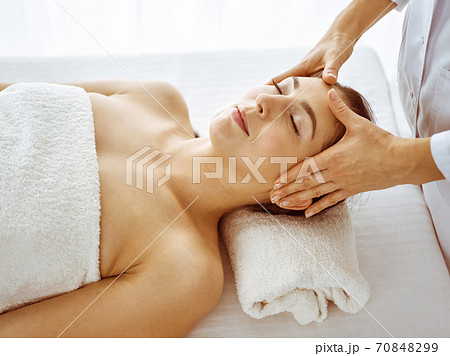 Beautiful brunette woman enjoying facial massage with closed eyes. Relaxing treatment in medicine and spa center concepts Beautiful brunette woman enjoying facial massage with closed eyes. Relaxing treatment in medicine and spa center concepts 70848299