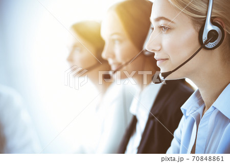 Call center and business people concept. Beautiful business woman with headphones consulting clients. Group of diverse phone operators at work in office Call center and business people concept. Beautiful business woman with headphones consulting clients. Group of diverse phone operators at work in office 70848861