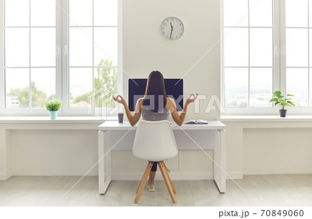 Woman taking break from work and meditating sitting at office table with computer and coffee 70849060