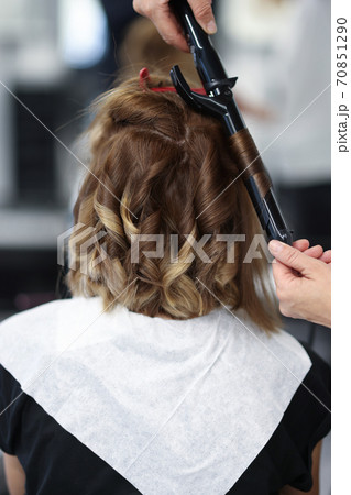 Woman in beauty salon is twisted curls of hair on curling iron. 70851290