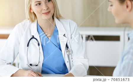 Woman-doctor and patient sitting and talking in sunny clinic. Blonde therapist is cheerfully smiling Woman-doctor and patient sitting and talking in sunny clinic. Blonde therapist is cheerfully smiling 70851673