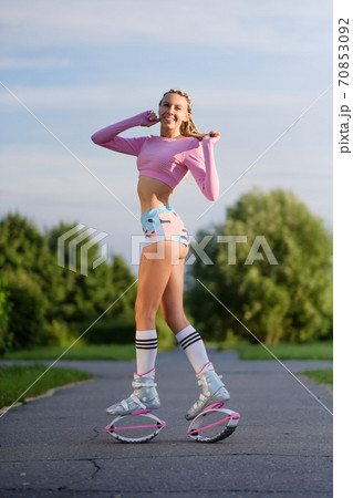 A young slender beautiful woman with dreadlocks in sportswear trains in the park outdoors. Kangoo jumps training. 70853092