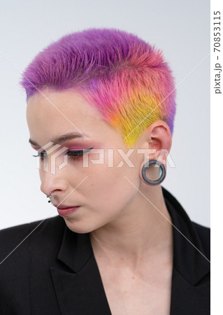 A young beautiful girl with short colored hair. Spread bright coloring and creative make-up. Piercing on the face. A black jacket. 70853115