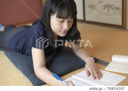 和室で寝ころびながら宿題をする女子高生の写真素材