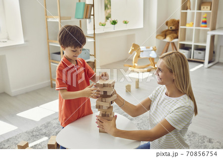 Happy mother shelping smiling son to build wooden pyramid of parts at home Happy mother shelping smiling son to build wooden pyramid of parts at home 70856754