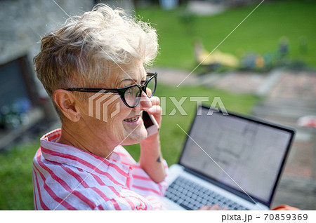 Senior woman architect with smartphone working outdoors in garden, home office concept. Senior woman architect with smartphone working outdoors in garden, home office concept. 70859369
