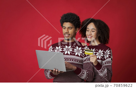 Smiling couple in sweaters buying gifts for family, african american young man with laptop and lady with credit card 70859622
