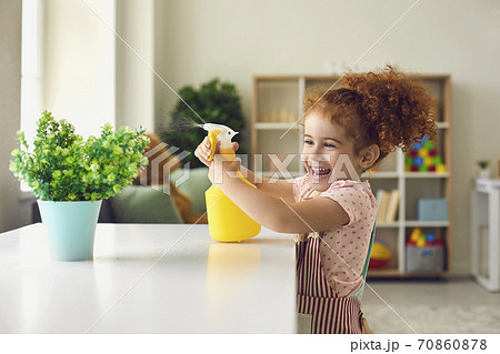 Little girl spraying water on houseplant at home. Cute child helping with household duties. Cheerful kid watering flower 70860878