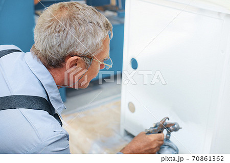 Painting of metal products. An elderly man paints a Cabinet with a compressor Painting of metal products. An elderly man paints a Cabinet with a compressor 70861362