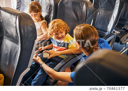 Flight attendant fastening a seatbelt of a happy boy Flight attendant fastening a seatbelt of a happy boy 70861377