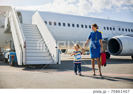 Flight attendant leading an unattended boy through the runway 70861407