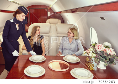Air hostess inside airplane serves first class passengers. Air hostess inside airplane serves first class passengers. 70864263