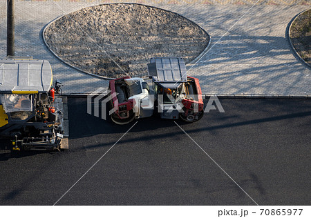 Industrial asphalt paver machine laying fresh asphalt and a Heavy road roller with vibration roller compactor press new hot asphalt on a road construction site. 70865977