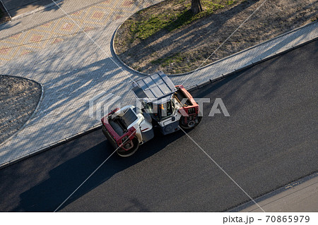 Asphalt road roller with heavy vibration roller compactor press new hot asphalt on the roadway on a road construction site. Heavy Vibration roller at asphalt pavement working. Repairing. 70865979