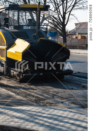 Industrial asphalt paver machine laying fresh asphalt on road construction site on the street. A Paver finisher placing a layer of a new hot asphalt on the roadway on a construction site. Repairing. 70866068
