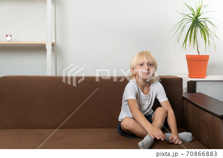 Smiling school-age boy sits on couch with his legs crossed. Free time for child Smiling school-age boy sits on couch with his legs crossed. Free time for child 70866883