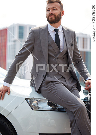 good-looking bearded business man sits on representative car hood good-looking bearded business man sits on representative car hood 70876900