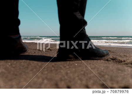 砂浜の男性の足 黒いズボン 靴と海の写真素材