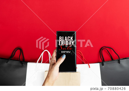 black friday sale, woman hand online shopping on smartphone with shopping bag on red background black friday sale, woman hand online shopping on smartphone with shopping bag on red background 70880426
