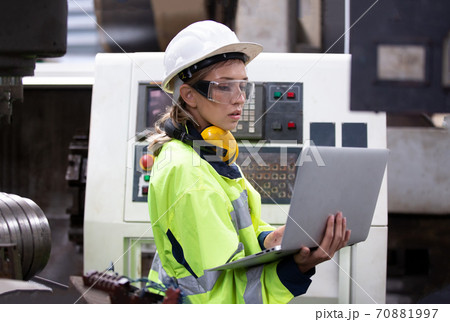 Female technician worker in uniform working on laptop with machine in manufacturing.	 70881997