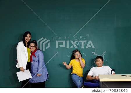 Teacher ,Asian girls with Down's syndrome and disabled boy on wheelchair in classroom with blackboard as background. Teacher ,Asian girls with Down's syndrome and disabled boy on wheelchair in classroom with blackboard as background. 70882346