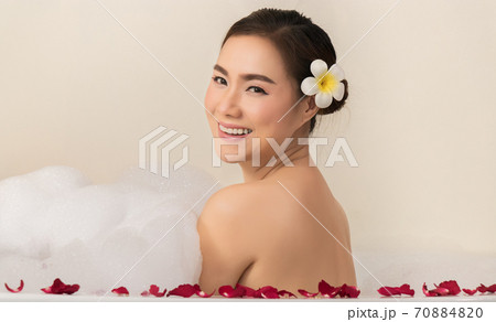 relaxing beautiful Asian woman pampering her body in water in a spa bathtub with white foam bubble of soap and rose petals. recreational pursuit relaxing beautiful Asian woman pampering her body in water in a spa bathtub with white foam bubble of soap and rose petals. recreational pursuit 70884820