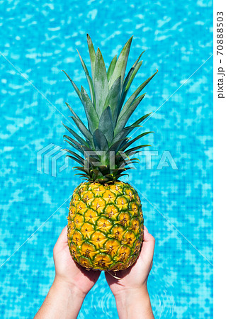 Pineapple in hand on swimming pool background. Pineapple in hand on swimming pool background. 70888503
