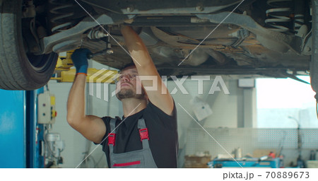 Auto mechanic working underneath car lifting machine at the garage. Auto repair shop, Car service, repair. 70889673