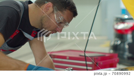 Close up footage of professional mechanic working on a vehicle in a car service. Engine specialist fixing the motor. Repairman is wearing gloves and using a ratchet. Close up footage of professional mechanic working on a vehicle in a car service. Engine specialist fixing the motor. Repairman is wearing gloves and using a ratchet. 70890992