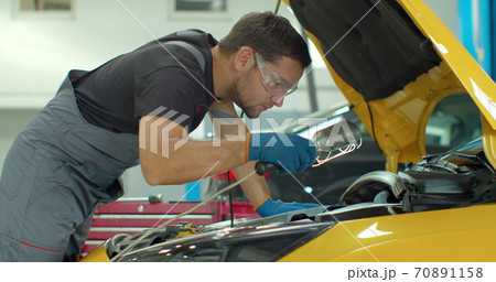 Mechanic man with lamp working at workshop. Car repair service. Professional mechanic is working on a car in a car service. 70891158