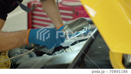 Repairman in safety glasses is working on an usual car maintenance. Professional mechanic is working on a car in a car service. He hangs a lamp and works with a ratchet. 70891186