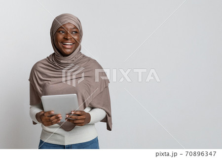 Joyful black muslim lady in hijabposing with digital tablet over light background Joyful black muslim lady in hijabposing with digital tablet over light background 70896347