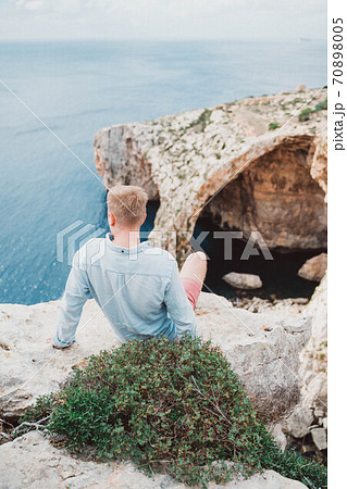 A man seating in front of a large rock. Watching to the sea. Nice weather. 70898005