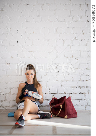 During a break in kickboxing training, a young pretty girl sits next to a wall and drinks water. During a break in kickboxing training, a young pretty girl sits next to a wall and drinks water. 70899073