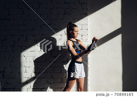 Beautiful contrasting portrait with the play of light and shadow of a young and fit girl in a loft interior with a white brick wall Beautiful contrasting portrait with the play of light and shadow of a young and fit girl in a loft interior with a white brick wall 70899165