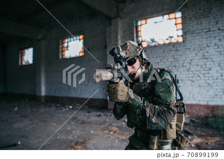 Military soldier in the form holds in the hands an assault rifle, check possible enemies around the corner Military soldier in the form holds in the hands an assault rifle, check possible enemies around the corner 70899199